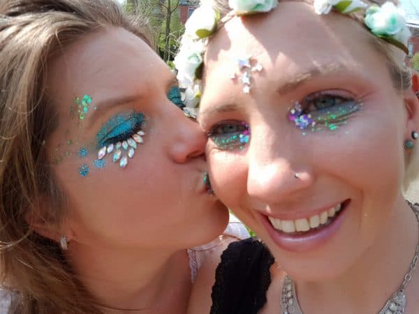 meisje geeft ander meisje kusje op de wang, beide met heel veel glitter op het gezicht